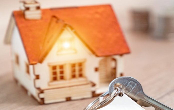 House key on a house shaped keychain resting on wooden floorboards concept for real estate, moving home or renting property
